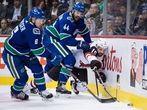 Defenceman Erik Gudbranson of the Vancouver Canucks staples Brad Richardson of the Arizona Coyotes to the boards while Brock Boeser takes control of the puck during Thursday's NHL game at Rogers Arena in Vancouver.