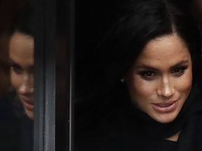 Meghan, Duchess of Sussex is reflected in a glass door as she leaves after a visit with her husband Britain's Prince Harry to the Old Vic Theatre in Bristol, England, Friday, Feb. 1, 2019.