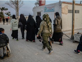 Veiled women, reportedly wives and members of the Islamic State, walk under the supervision of a female fighter from the Syrian Democratic Forces (SDF) at al-Hol camp at al-Hasakeh governorate at northeastern Syria on February 17, 2019.