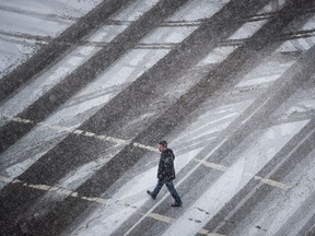 A man crosses a street as snow falls in Vancouver, B.C.