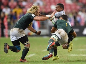 Fiji's Napolioni Bolaca runs with the ball, stiff-arming South Africa's Werner Kok (left) while Chris Dry (right) tackles during the Singapore Rugby Sevens Cup final match between South Africa and Fiji in Singapore on April 14, 2019.