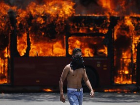 An anti-government protester walks near a bus that was set on fire by opponents of Venezuela's President Nicolas Maduro during clashes between rebel and loyalist soldiers in Caracas, Venezuela, Tuesday, April 30, 2019.