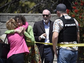 Two people hug as another talks to a San Diego County Sheriff's deputy outside of the Chabad of Poway Synagogue in Poway, Calif.