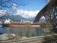 Oil tanker Erik Spirit moves under the Second Narrows Bridge, escorted by a tug (covered by plants in foreground), on March 30, 2019.