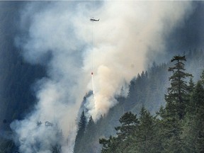 A helicopter dumps sea water on a wildfire, about three hectares in size near the Sea to Sky Highway in West Vancouver, BC.