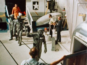The Apollo 11 crewmen, wearing biological isolation garments, arrive aboard the USS Hornet during recovery operations in the central Pacific. They're followed by flight surgeon Dr. Bill Carpentier, dressed in an orange flight suit.