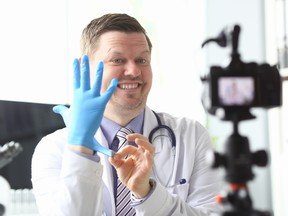 A doctor puts on his glove infront of a propped-up camera. Doctors are divided on whether to let patients record their own surgeries on their phones.