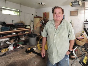 Ken Rechik stands in his garage with the hole in the ceiling raccoons used to access his garage behind him to his right, and the small window they climbed through to gain entry to his home over his left shoulder.