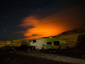 A trailer parked at a campground in Savona in the B.C. Interior is seen as the Elephant Hill wildfire burns in the distance near Clinton, illuminating smoke in the sky during the early morning hours of July 30, 2017.