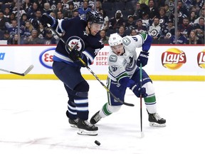 Troy Stecher of the Vancouver Canucks battles for puck possession with Joona Luoto of the Jets during Friday's NHL game in Winnipeg. Says Stecher of his team's early identity: "We know who we are."