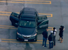 A screenshot of aerial footage showing authorities, on the top level of the parkade, gathered around the black vehicle with three of its doors left open. The woman and two children were found dead on the pavement below.