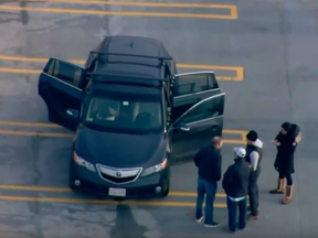 A screenshot of aerial footage showing authorities, on the top level of the parkade, gathered around the black vehicle with three of its doors left open. The woman and two children were found dead on the pavement below.