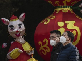 Chinese men wear protective masks as they walk by a decoration marking the Year of the Rat in a park after celebrations for the Chinese New Year and Spring Festival were cancelled by authorities on Jan. 25, 2020 in Beijing, China.