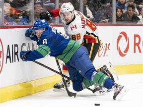 Brock Boeser of the Vancouver Canucks gets checked into the end boards while battling for a loose puck against Andrew Mangiapane of the Calgary Flames on February 8, 2020. Boeser suffered a rib cartilage fracture in the game and is expected to miss eight weeks of action.