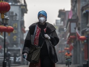 A Chinese woman wears a protective mask and gloves as she walks in a nearly empty and shuttered commercial street on February 12, 2020 in Beijing, China.