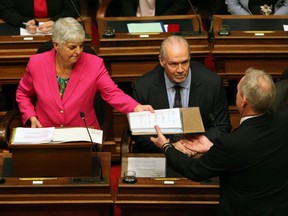 B.C. Premier John Horgan looks on as Minister of Finance Carole James passes on a copy of the B.C. budget before she delivers her speech from the legislative assembly in Victoria on Feb. 18.