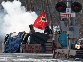 A protester stands beside smoke at the closed train tracks in Tyendinaga Mohawk Territory near Belleville, Ont., on Feb. 20, 2020.
