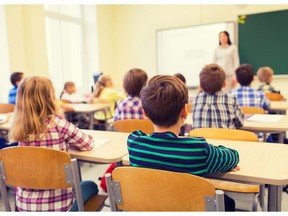 education, elementary school, learning and people concept - group of school kids sitting and listening to teacher in classroom from back