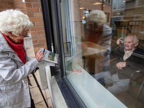 Hilda Duddridge, 95, shows her husband Lew Duddridge ,102, his daily Times Colonist newspaper while on a visit through glass at Selkirk Place in Victoria, B.C.