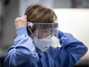 Katie Kempton, a laboratory technologist at LifeLabs, wears a face mask as she adjusts a face shield while putting on protective equipment before demonstrating how a specimen is tested for COVID-19 at the company's lab, in Surrey, B.C., on Thursday, March 26, 2020. LifeLabs is Canada's largest private provider of diagnostic testing for health care.