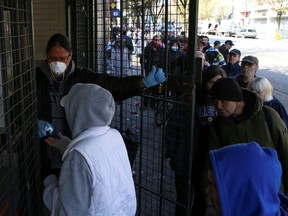 A staff member sanitizes a customer's hands at Pigeon Park Savings, a bank that caters to low-income residents of Vancouver's Downtown Eastside and where people gather in large numbers to collect their social assistance cheques, as the number of COVID-19 cases continues to grow March 25 in Vancouver.