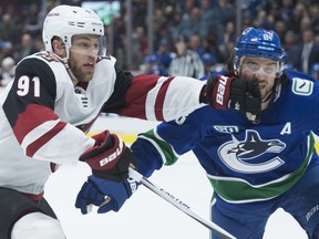 Arizona Coyotes winger Taylor Hall gets his glove in the face of Vancouver Canucks defenceman Chris Tanev while they both chase the puck during a Jan. 16, 2020 NHL game at Rogers Arena in Vancouver.