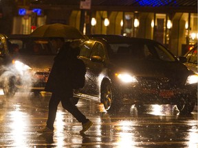 A pedestrian crosses the street during a rainy night in Vancouver.