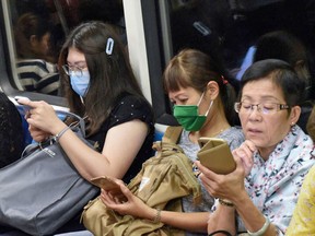Commuters wearing face masks as a preventive measure against the COVID-19 coronavirus look at their mobile phones on the Mass Rapid Transit train in Singapore on March 18, 2020.