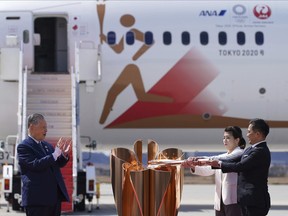 Three-time Olympic gold medalists Tadahiro Nomura, right, and Saori Yoshida light the torch as Tokyo 2020 Olympics chief Yoshiro Mori, left, watches during Olympic Flame Arrival Ceremony at Japan Air Self-Defense Force Matsushima Base in Higashimatsushima in Miyagi Prefecture, north of Tokyo, Friday, March 20, 2020.