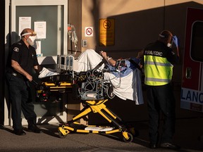 Paramedics in personal protective equipment move a patient from an ambulance into Royal Columbian Hospital in New Westminster.