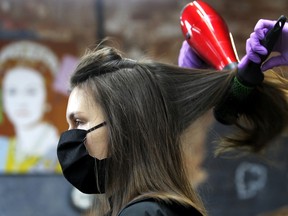 An employee dries the hair of a customer wearing a protective face mask. Some salons are calling for mandatory training to reopen post-COVID-19.