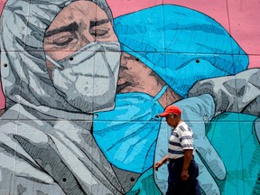 In this file photo taken on May 1, 2020 a man walks past a coronavirus-related mural, in Acapulco, Guerrero State, Mexico, amid the COVID-19 pandemic