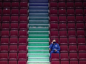 Head coach Travis Green, with a face mask and clipboard, watches his Vancouver Canucks workout from the stands in Rogers Arena.