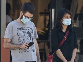 Pedestrians wearing masks wait to cross the street in Vancouver.