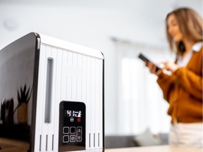 Close-up on a smart air humidifier with touch screen, woman controlling it with smart phone on the background