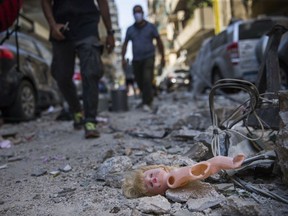 People walk past a child's doll that was blown out of a nearby building after a massive explosion, which occurred a day before, on Aug. 5, 2020 in Beirut, Lebanon.