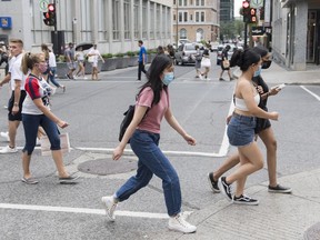 People wear face masks as they cross a street in Montreal, Sunday, August 9, 2020, as the COVID-19 pandemic continues in Canada and around the world. Government and public health officials need to empower people in their 20s to reduce the risk of contracting COVID-19, instead of blaming and shaming them for disproportionately representing new infections across the country, say experts.