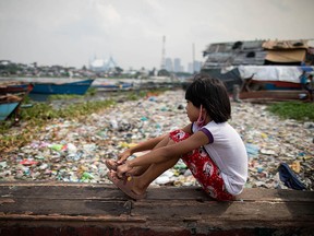 A Filipino girl sits on a piece of wood as she looks out to a trash-filled Manila Bay near their shanty home, amid the COVID-19 outbreak.