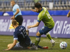 Seattle Sounders FC midfielder Joao Paulo  avoids a slide tackle by Vancouver Whitecaps midfielder Andy Rose during the first half of a 2020 Major League Soccer game at CenturyLink Field.
