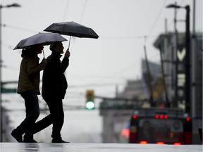 In this file photo, pedestrians brave the wind and rain in Vancouver, BC.