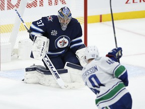 Winnipeg Jets goaltender Connor Hellebuyck (37) gets his elbow on the shot from Vancouver Canucks' Elias Pettersson (40) during second period NHL action in Winnipeg on Saturday, January 30, 2021.