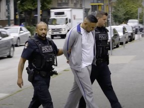 ary Kang is pictured in cuffs being escorted by two Vancouver police officers on Aug. 7, 2018, in Vancouver. He was shot dead in his parents' home in Surrey.