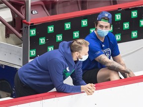 Vancouver Canucks' Alexander Edler, left, of Sweden, and Jake Virtanen wears face masks as they talk on the bench at training camp this week. The Canucks have cancelled a practice initially scheduled for Sunday following a possible exposure to COVID-19.