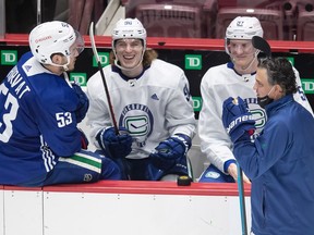 Vancouver Canucks' Adam Gaudette, second left, laughs while sitting on the bench with Bo Horvat, left, and Tyler Myers as head coach Travis Green, front right, stands on the ice during the NHL hockey team's training camp in Vancouver, on Friday, January 8, 2021.