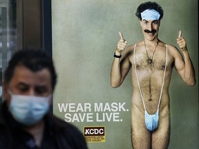 A person wearing a mask walks past a bus stop ad on 5th Avenue, October 15, 2020, for the movie "Borat 2," featuring actor Sacha Baron Cohen, ahead of its release on October 23.