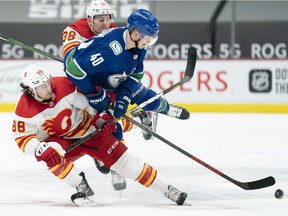 Vancouver Canucks centre Elias Pettersson (40) fights for control of the puck with Calgary Flames left wing Andrew Mangiapane (88) and Byron Froese (38) during first period NHL action in Vancouver, Monday, February 15, 2021.