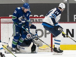 Canucks captain Bo Horvat winces in reaction after getting hit with the puck while standing in front of Winnipeg Jets goalie Connor Hellebuyck during the third period of Monday’s NHL game at Rogers Arena.