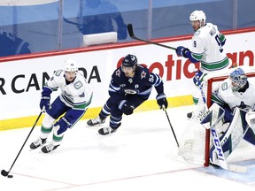 Canucks centre Elias Pettersson shields the puck from a chasing Mark Scheifele of the Winnipeg Jets while goalie Thatcher Demko holds his post during their March 1, 2021 NHL game in Winnipeg.