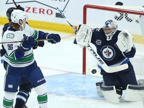 Adam Gaudette runs interference in front of Winnipeg Jets goalie Connor Hellebuyck during the Canucks-Jets NHL game in Winnipeg on Monday.