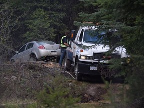 A car is hauled from the bush Monday night off the Arawana Forest Service Road near Penticton. Police were called to a report of "suspicious circumstances" on the road Monday around the same time two dead bodies were found on nearby Naramata Creek forest service road.